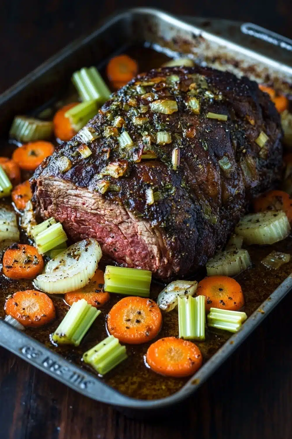 Slow cooker beef chuck roast - the image shows a large piece of cooked meat on a baking tray. the meat appears to be a medium-rare ribeye steak, with a dark brown crust on top. it is garnished with chopped onions and celery, and there are also small pieces of carrots and onions scattered around the dish. the tray is sitting on a wooden table, and the background is blurred, making the meat the focal point of the image.