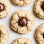 Sugar cookie kisses - the image shows a group of freshly baked cookies on a white surface. the cookies are round and golden brown in color, with a crumbly texture. they are arranged in a scattered manner, with some overlapping each other. some of the cookies have a bite taken out of one of them, revealing the chocolate filling inside. the chocolate filling is a dark brown color and appears to be in the shape of a letter "m". the cookies appear to be soft and chewy, and the texture is slightly uneven.