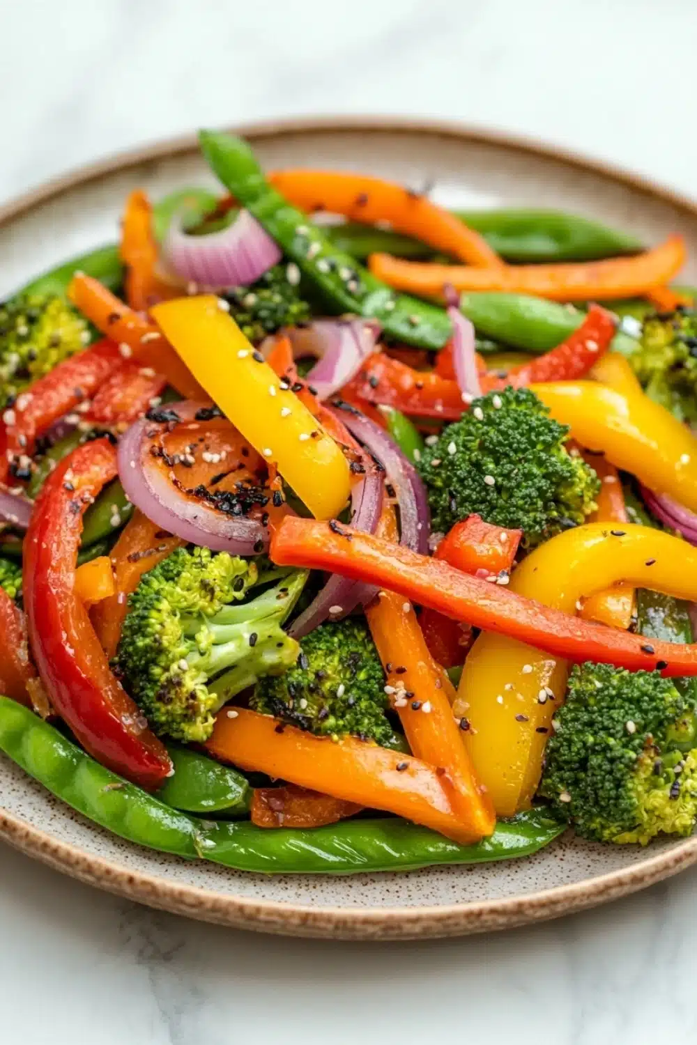 Thai vegetable air fryer - the image is a close-up of a plate of stir-fry dish. the dish is made up of various vegetables, including broccoli, red bell peppers, and green beans. the vegetables are arranged in a colorful and appetizing manner, with some overlapping each other. the colors of the vegetables are vibrant and the dish appears to be fresh and healthy. the plate is made of a light-colored ceramic or porcelain material and is sitting on a white marble countertop.