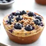 Blueberry muffin pancake bowl - the image shows a close-up of a blueberry tart on a baking tray. the tart has a golden brown crust and is topped with fresh blueberries. the blueberries are arranged in a crumbly manner on top of the tart, with some of them overlapping each other. in the background, there is a small bowl of more blueberries, suggesting that the tart is ready to be served. the tray is on a white countertop.