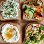 Bread toppings - the image shows four slices of bread arranged on a wooden cutting board. each slice has a different type of food on it. the first slice on the top left is topped with a dollop of white cream cheese and garnished with chopped herbs. the second slice in the middle is filled with sliced cucumbers, carrots, and sun-dried tomatoes. the third slice is covered in a creamy white sauce with a runny yolk. the fourth slice is filled to the brim with a mixture of chickpeas, avocado, and basil. all four slices are arranged in a neat and orderly manner, with the bread on the left slightly overlapping the one on the right. the background is a light-colored wooden table.