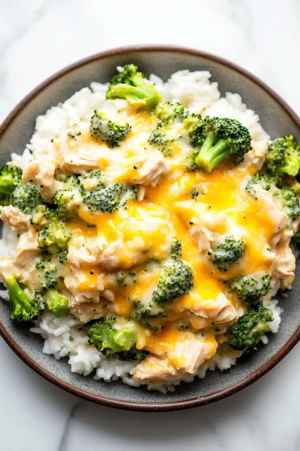 Chicken broccoli casserole slow cooker - the image is a close-up of a bowl of food. the bowl is made of dark brown ceramic and is placed on a white marble countertop. the food in the bowl appears to be a dish made with rice and broccoli. the rice is white and fluffy, and the broccoli is bright green. on top of the rice, there is a layer of melted cheese, which is a light yellow color. the cheese is spread evenly over the top, covering the entire dish. the dish looks appetizing and ready to eat.