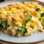Chicken broccoli casserole with panko - the image shows a plate of food with a serving of chicken and broccoli casserole. the plate is white with a speckled pattern and is placed on a white tablecloth. the chicken is covered in a layer of melted cheese and crumbled breadcrumbs, giving it a golden brown color. the broccoli pieces are bright green and appear to be cooked until they are soft and fluffy. the dish looks appetizing and ready to eat.
