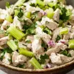 Chicken salad finely chopped - the image is a close-up of a bowl of salad. the bowl is made of ceramic and is sitting on a white marble countertop. the salad is made up of diced chicken, celery, and red onions, and is garnished with fresh cilantro. the chicken appears to be seasoned with herbs and spices, and the celery is cut into small pieces. the red onions are scattered throughout the salad, adding a pop of color to the dish.
