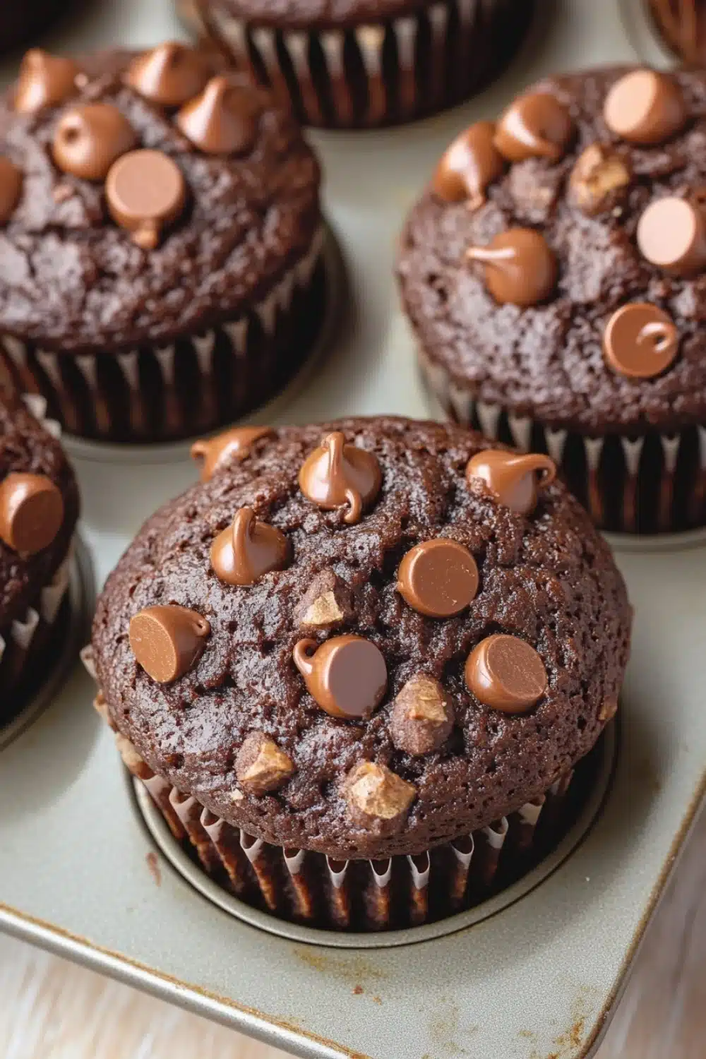 Chocolate muffin without eggs - the image shows a tray of freshly baked chocolate muffins. the muffins are round and have a golden brown color. they are topped with chocolate chips and peanut butter cups. the tray is lined with parchment paper and is placed on a wooden surface. the background is blurred, but it appears to be a kitchen countertop.