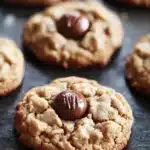 Cookie peanut butter hersheys kisses - the image shows a tray of freshly baked cookies on a black baking tray. the cookies are round and golden brown in color, with a crumbly texture. they are arranged in a single layer on the tray, with some overlapping each other. in the center of each cookie, there is a chocolate-covered cookie with a drizzle of chocolate on top. the background is blurred, but it appears to be a kitchen countertop.
