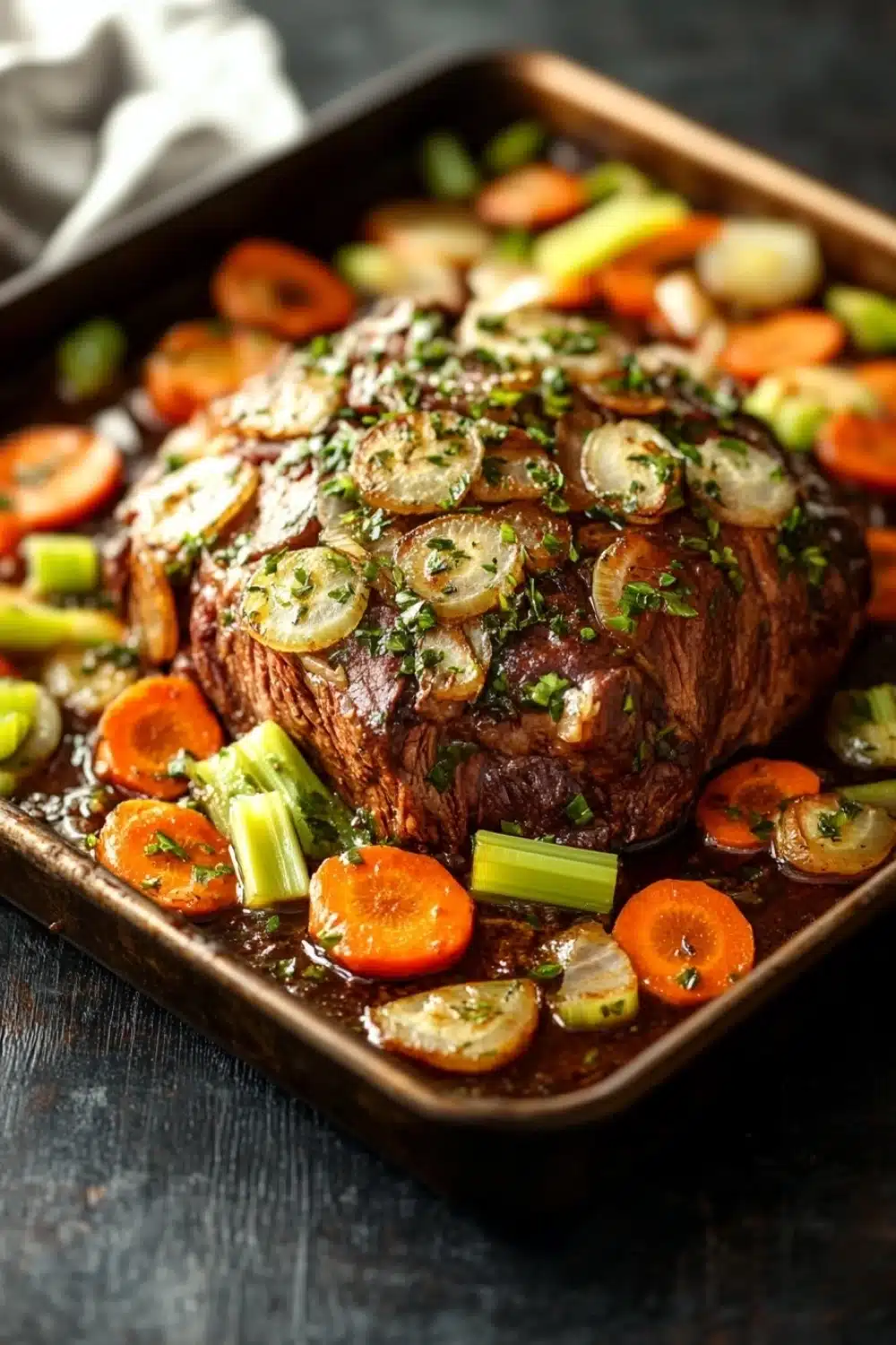 French roast beef slow cooker - the image shows a large rectangular baking dish filled with a dish of cooked meat. the meat appears to be a roast beef, with a dark brown color and a shiny texture. it is garnished with chopped herbs and sliced carrots and celery. the dish is served on a dark wooden table with a white cloth napkin on the side. the vegetables are arranged in a circular pattern around the meat, with some overlapping each other. the overall appearance of the dish is savory and appetizing.