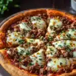 Frozen deep dish pizza - the image is of a freshly baked pizza on a wooden cutting board. the pizza has a golden brown crust and is topped with melted cheese and chunks of ground beef. the cheese is melted and bubbly, and there are small chunks of red sauce scattered throughout the pizza. on the right side of the image, there is a small bowl of sour cream and a sprig of parsley. the background is blurred, but it appears to be a kitchen countertop.