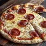 Gluten free pizza crust psyllium husk - the image shows a pepperoni pizza on a wooden cutting board. the pizza is round and has a golden brown crust. it is topped with melted cheese and several slices of pepperoni arranged in a circular pattern. the pepperoni is red and appears to be freshly baked. the cutting board is placed on a dark wooden table with a rustic background.