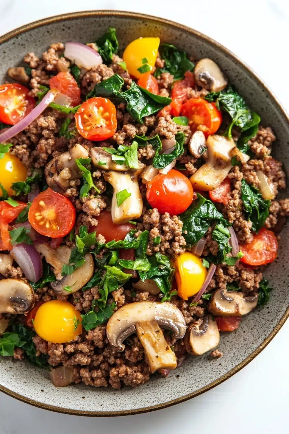 Ground beef for dinner main dishes - the image is a close-up of a bowl of food. the bowl is made of dark brown ceramic and is placed on a white marble countertop. the food appears to be a salad with a variety of ingredients, including diced tomatoes, sliced mushrooms, red onions, and green leafy vegetables. the tomatoes are bright red and appear to be ripe and juicy, while the mushrooms are sliced and have a light brown color. the greens are a mix of green and red, and they are scattered throughout the dish. the dish looks fresh and appetizing.