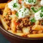 Ground turkey for dinner casseroles pasta - the image is a close-up of a bowl of pasta dish. the pasta appears to be penne, which is a type of penne pasta, and it is cooked in a tomato-based sauce. the dish is topped with chunks of ground meat, possibly ground beef, and a dollop of sour cream. the sauce is a deep red color and is drizzled over the top of the pasta. there are also a few sprigs of fresh parsley scattered throughout the dish, adding a pop of green color. the bowl is made of dark brown ceramic and is sitting on a dark blue surface.