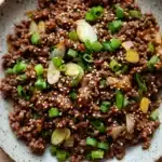 Korean beef skillet - the image is a close-up of a bowl of food. the bowl is made of a light-colored ceramic with a speckled pattern. the food appears to be a dish made with ground beef, sliced green onions, and small pieces of yellow squash. the ground beef is dark brown and looks crispy on the outside. the onions are cut into small cubes and are scattered throughout the dish. the green onions are bright green and look fresh and vibrant. the yellow squash is cut into thin slices and is placed on top of the ground beef. the dish is garnished with sesame seeds, giving it a crunchy texture.