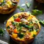 Low cal freezer breakfast - the image shows a close-up of a quiche on a baking tray. the quiche is golden brown and has a flaky crust. it is filled with a mixture of scrambled eggs, sausage, mushrooms, red bell peppers, and green spinach. the sausage is cooked to a medium-rare and appears to be seasoned with herbs and spices. the mushrooms are sliced and arranged in a circular pattern on top of the quiche. the spinach is scattered around the tray, adding a pop of green color to the dish. the tray is lined with a few sprigs of parsley.