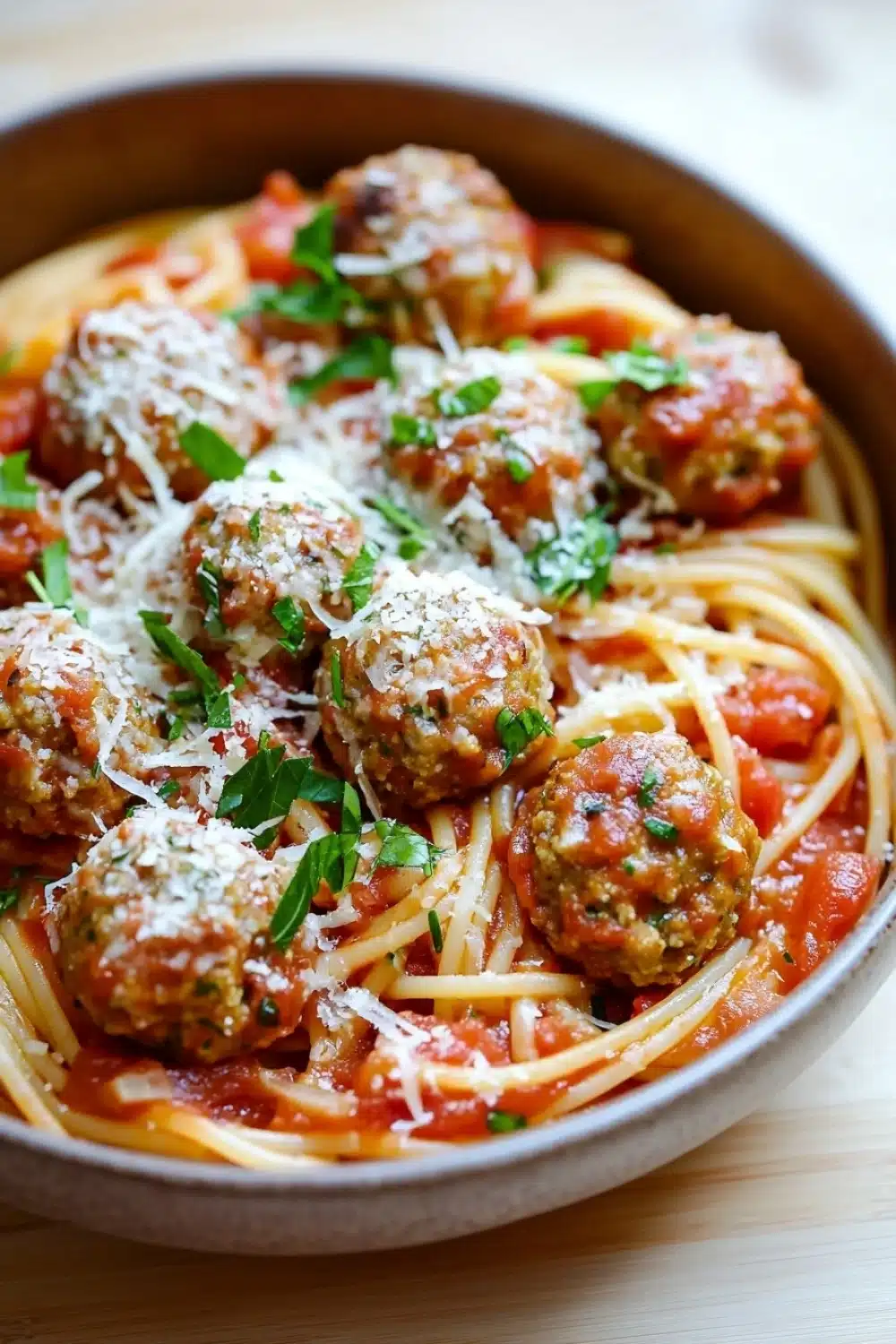 Make ahead pasta and meatballs - the image shows a bowl of spaghetti and meatballs. the spaghetti is cooked al dente and is covered in a tomato sauce. the meatballs are golden brown and appear to be seasoned with herbs and grated cheese. the dish is garnished with fresh parsley. the bowl is made of ceramic and is sitting on a wooden table.