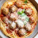 Make ahead pasta and meatballs - the image shows a bowl of spaghetti and meatballs. the spaghetti is cooked al dente and is covered in a red tomato sauce with chunks of meatballs scattered throughout. the meatballs are golden brown and appear to be seasoned with grated parmesan cheese. the dish is garnished with fresh basil leaves. the bowl is made of ceramic and is sitting on a white countertop.