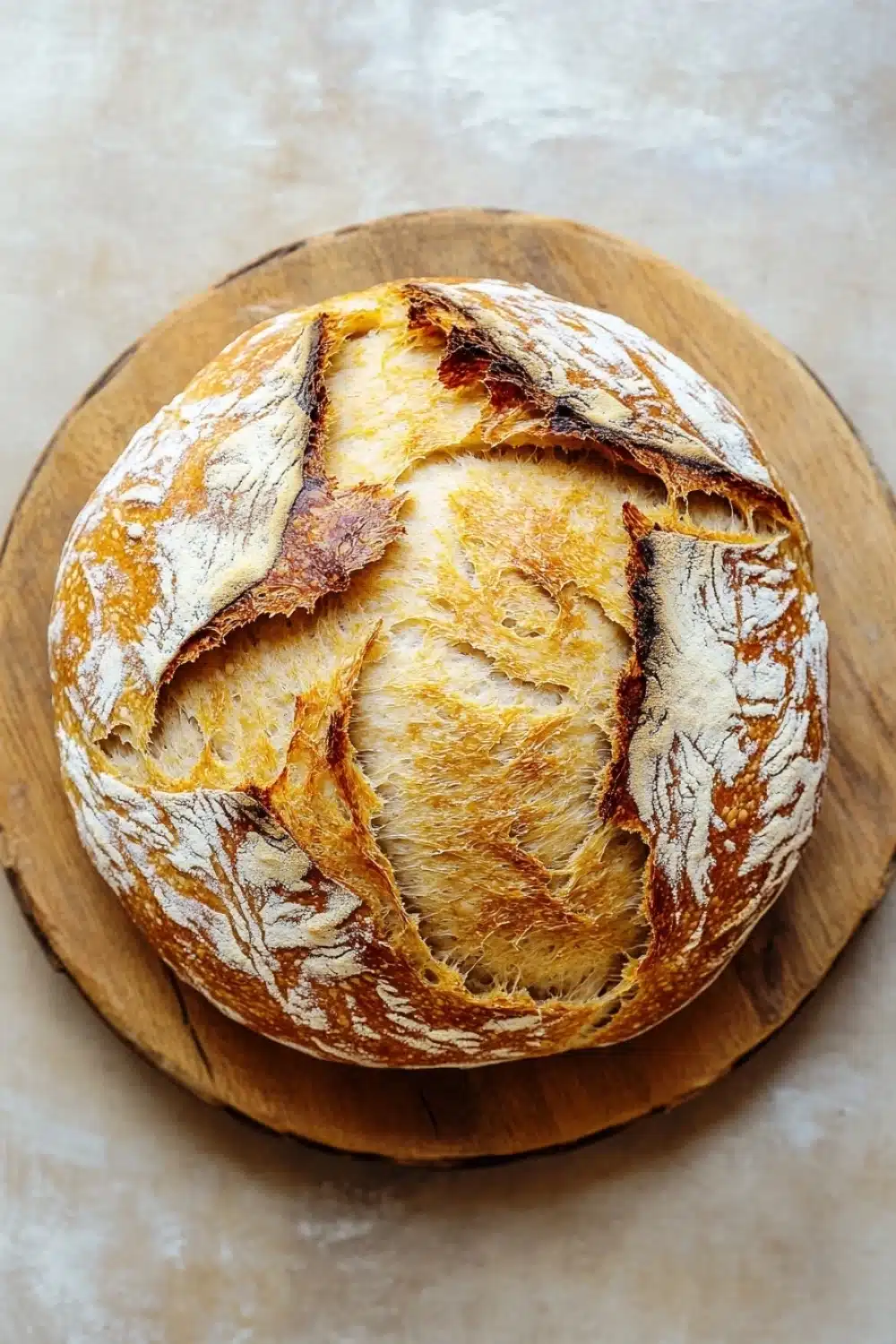 No knead bread dutch oven 2 hour - the image is a close-up of a freshly baked loaf of bread on a wooden cutting board. the bread appears to be freshly baked, with a golden-brown crust and a soft, fluffy interior. the edges of the bread are slightly frayed, indicating that it has been freshly baked. the cutting board is placed on a beige-colored surface, possibly a table or countertop. the background is blurred, making the bread the focal point of the image.