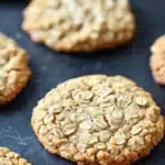 Oatmeal cookies - the image shows a group of freshly baked oatmeal cookies on a black baking tray. the cookies are round and golden brown in color, with a crumbly texture on top. they are arranged in a scattered manner, with some overlapping each other. the tray appears to be lined with parchment paper, and the background is blurred, making the cookies the focal point of the image.