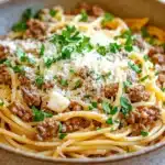 One pot garlic butter pasta with beef - the image is a close-up of a bowl of spaghetti bolognese. the spaghetti is cooked al dente and is topped with a generous amount of minced meat and grated parmesan cheese. the dish is garnished with fresh parsley. the bowl is made of ceramic and is sitting on a wooden table. the background is blurred, but it appears to be a kitchen countertop.