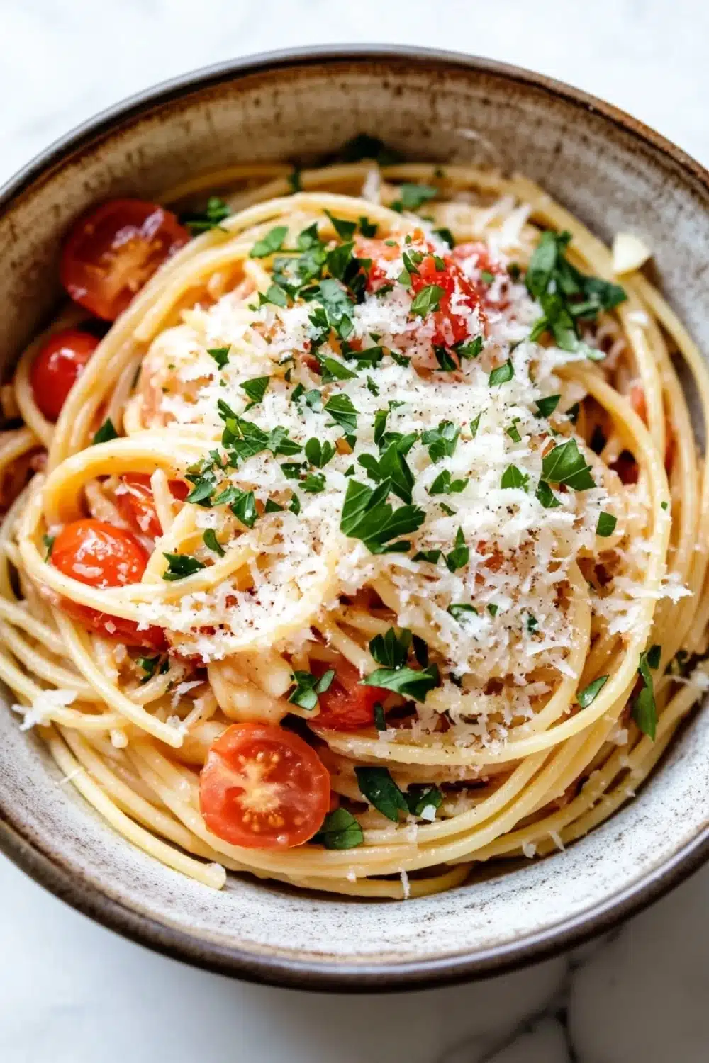 One pot pasta and dutch oven - the image is a close-up of a bowl of spaghetti dish. the bowl is made of ceramic and has a light brown color. the spaghetti is cooked al dente and is topped with a generous amount of grated parmesan cheese and fresh herbs. there are also sliced cherry tomatoes scattered throughout the dish, adding a pop of color and texture. the dish is garnished with a sprig of fresh parsley. the background is a white marble countertop.