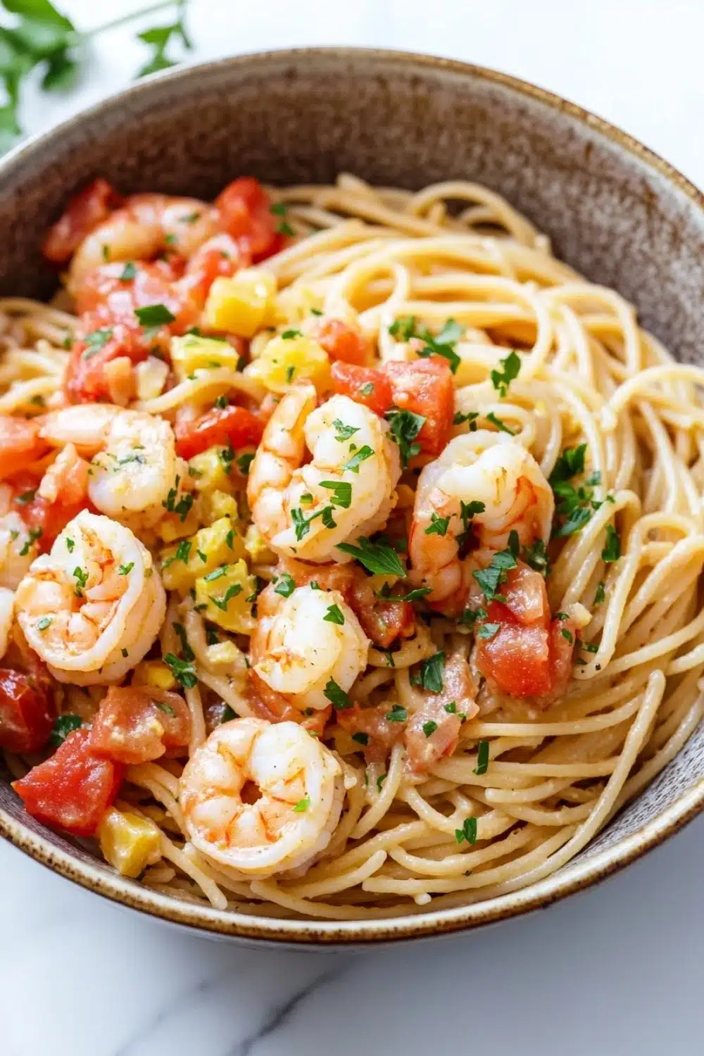 One pot pasta crevette - the image is a close-up of a bowl of spaghetti with shrimp and tomato sauce. the spaghetti is cooked al dente and is topped with chunks of shrimp, diced tomatoes, and chopped herbs. the dish is garnished with a sprig of parsley. the bowl is made of ceramic and is sitting on a white marble countertop. the background is blurred, making the dish the focal point of the image.