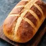 Red star rise yeast bread - the image shows a freshly baked loaf of bread on a wooden cutting board. the bread is golden brown in color and has a criss-cross pattern on its surface. the loaf appears to be freshly baked and is sitting on a dark grey countertop. the cutting board is made of dark wood and is placed next to the bread. the background is blurred, but it seems to be a kitchen countertop with a white cloth napkin on the right side.