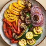 Sauteed vegetables on grill - the image is a close-up of a plate of grilled vegetables. the plate is round and has a light brown color with a speckled pattern. on the plate, there are sliced red and yellow bell peppers, sliced zucchini, and sliced mushrooms. the vegetables are arranged in a circular pattern and appear to be seasoned with herbs and spices. the background is a wooden table.