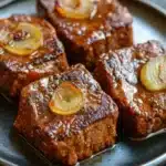 Slow cooker beef cube steak - the image shows four square-shaped pieces of meatloaf on a black plate. the meat appears to be cooked and has a golden brown color. each piece is garnished with sliced onions on top, giving it a fresh and appetizing appearance. the plate is sitting on a dark grey countertop, and the background is blurred, making the meat and onions the focal point of the image.
