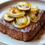 Slow cooker beef cube steak - the image shows a plate of food with a piece of steak on it. the steak appears to be cooked medium-rare and has a dark brown crust on the outside. on top of the steak, there are sliced onions arranged in a circular pattern. the onions are golden brown and appear to be seasoned with herbs and spices. the plate is white with a speckled pattern and is sitting on a wooden table. the background is blurred, but it seems to be a kitchen countertop.