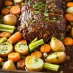 Slow cooker pot roast and vegetables - the image shows a baking tray filled with a dish of beef and vegetables. the beef appears to be cooked medium-rare and is covered in a rich, dark brown sauce. the vegetables include carrots, potatoes, and celery. the tray is lined with parchment paper and is placed on a white marble countertop. the dish looks appetizing and ready to be served.