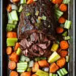 Slow cooker pot roast beef - the image shows a rectangular baking dish filled with a dish of cooked beef and vegetables. the beef appears to be medium-rare and has a dark brown color. it is garnished with chopped celery and sliced carrots. the vegetables are arranged around the beef, with some of them overlapping each other. the dish is sitting on a dark grey countertop. the overall appearance of the dish is savory and appetizing.
