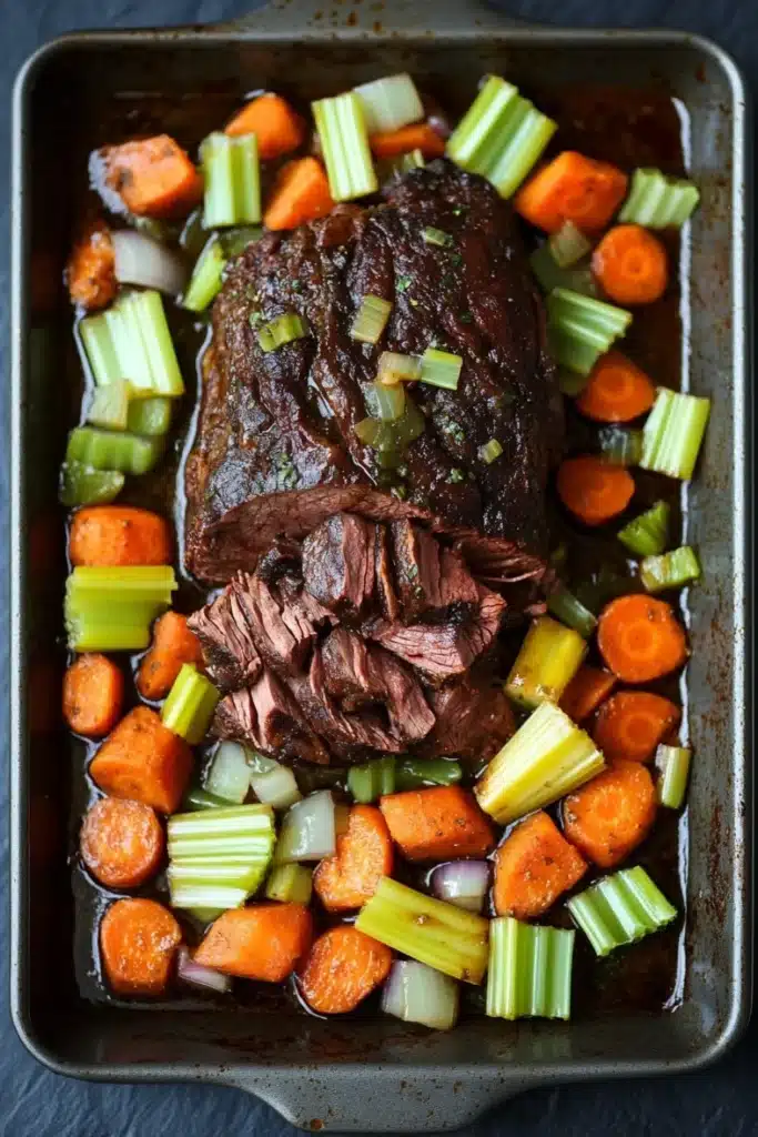 Slow cooker pot roast beef - the image shows a rectangular baking dish filled with a dish of cooked beef and vegetables. the beef appears to be medium-rare and has a dark brown color. it is garnished with chopped celery and sliced carrots. the vegetables are arranged around the beef, with some of them overlapping each other. the dish is sitting on a dark grey countertop. the overall appearance of the dish is savory and appetizing.