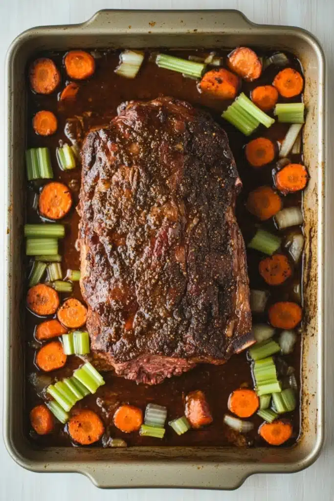 Slow cooker roast beef from frozen - the image shows a rectangular baking dish with a large piece of cooked meat in the center. the meat appears to be a medium-rare ribeye steak, with a dark brown crust on top. it is surrounded by a bed of sliced carrots and celery. the carrots are bright orange and appear to be cooked until they are soft and tender. the celery is a bright green color and is arranged in a circular pattern around the meat. the dish is sitting on a white countertop.