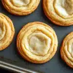 Sugar cookie mix - the image shows a baking tray lined with freshly baked cookies. the cookies are round and golden brown in color, with a swirl pattern on top. they are arranged in a single layer on the tray, with some overlapping each other. the background is dark, making the cookies stand out.
