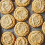 Sugar cookie platter - the image shows a tray of freshly baked cookies on a wooden table. the cookies are round and golden brown in color, with a crumbly texture on top. they are arranged in a single layer on the tray, with some overlapping each other. the tray is lined with parchment paper, and the cookies appear to be freshly baked. the background is blurred, but it appears to be a rustic wooden surface.