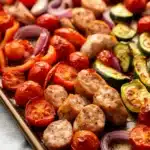 Trader joes chicken sausage sheet pan - the image shows a baking tray filled with a variety of vegetables. on the left side of the tray, there are sliced tomatoes, red onions, and zucchini. in the center, there is a pile of grilled chicken skewers. the chicken appears to be seasoned with herbs and spices, and the vegetables are arranged in a colorful and appetizing manner. the tray is lined with parchment paper and is sitting on a white tablecloth.