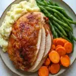 Turkey dinners - the image shows a plate of food on a white marble countertop. on the left side of the plate, there is a serving of mashed potatoes with green beans and sliced carrots. the mashed potatoes are golden brown and appear to be seasoned with herbs and spices. the green beans are bright green and look fresh and vibrant. the carrots are cut into small cubes and are arranged in a pile on the plate. the plate is round and has a beige rim.