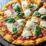 Zucchini crust pizza keto - the image is of a freshly baked pizza on a wooden cutting board. the pizza has a golden brown crust and is topped with melted cheese and fresh basil leaves. the cheese is melted and bubbly, and the basil leaves are arranged in a circular pattern around the edges of the pizza. the background is a dark wooden table with a white cloth napkin on the side. the overall aesthetic of the image is rustic and appetizing.