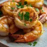 Air fryer shrimp cooking time - the image shows a plate of cooked shrimp. the shrimp are golden brown and appear to be seasoned with herbs and spices. they are arranged in a circular pattern on the plate, with some overlapping each other. the plate is white with a speckled texture, and there are a few sprigs of parsley scattered around the plate. the background is blurred, but it appears to be a wooden table or countertop.