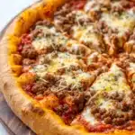 At home deep dish pizza - the image is of a freshly baked pizza on a wooden cutting board. the pizza has a golden brown crust and is topped with melted cheese, red sauce, and chunks of ground meat. the cheese is melted and bubbly, and there are small flecks of herbs scattered throughout the pizza. the background is a white marble countertop.