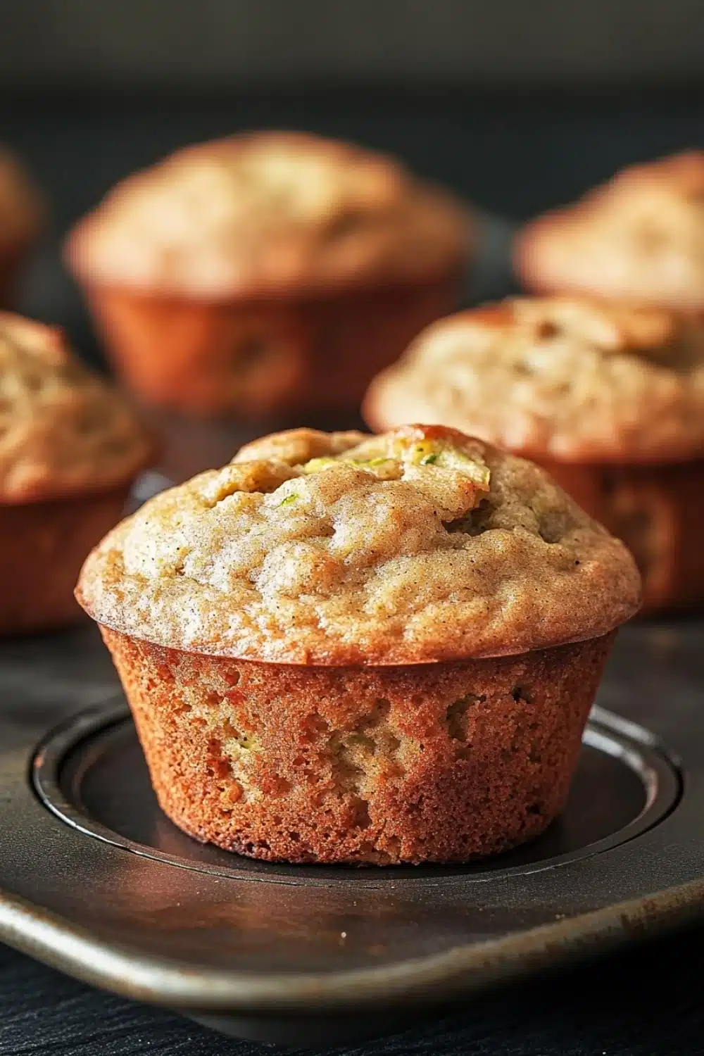 Banana muffin with applesauce and zucchini - the image shows a group of freshly baked muffins on a black baking tray. the muffins are golden brown in color and have a crumbly texture. one of the muffins has a bite taken out of it, revealing the soft, fluffy interior. the tray is lined with parchment paper and there are a few more muffins visible in the background. the overall mood of the image is warm and inviting.