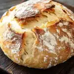 Bread to go with chili - the image is a close-up of a freshly baked loaf of bread on a wooden cutting board. the bread appears to be golden brown in color and has a soft, fluffy texture. the top of the bread is covered in a layer of powdered sugar, giving it a shiny appearance. the cutting board is placed on a dark wooden table with a blue cloth napkin on the side. the background is blurred, making the bread the focal point of the image.