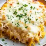 Cheesy chicken spaghetti squash casserole jar of lemons - the image shows a slice of spaghetti squash casserole on a white plate. the dish is golden brown and has a layer of melted cheese on top. the cheese is melted and bubbly, and there are small pieces of chicken scattered throughout the dish. the plate is garnished with chopped parsley. the background is blurred, but it appears to be a wooden table.