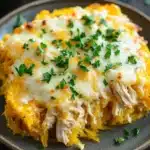 Cheesy chicken spaghetti squash casserole jar of lemons - the image shows a plate of spaghetti squash casserole with a layer of melted cheese on top. the cheese is golden brown and appears to be melted and bubbly. the dish is garnished with fresh parsley. the plate is on a wooden table with a green casserolle in the background. the overall color scheme of the image is warm and inviting.