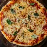 Chicago style thin crust pizza dough - the image is of a freshly baked pizza on a wooden cutting board. the pizza is round and has a golden brown crust. it is topped with melted cheese, red sauce, and fresh basil leaves. the cheese is melted and bubbly, and there are small chunks of tomato sauce scattered throughout the pizza. the cutting board is placed on a dark wooden table, and the background is blurred, making the pizza the focal point of the image.