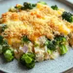 Chicken broccoli casserole dinner - the image shows a plate of food with a casserole dish on it. the dish appears to be made with broccoli and chicken, and it is topped with a layer of melted cheese. the cheese is golden brown and bubbly, and there are small pieces of broccoli scattered throughout the dish. the plate is white with a speckled pattern, and a fork is visible on the right side of the image. the background is a wooden table.