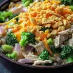 Chicken broccoli casserole mushroom soup - the image is a close-up of a bowl of food. the bowl is made of dark brown ceramic and is sitting on a dark grey countertop. the food appears to be a stir-fry with broccoli, chicken, and other vegetables mixed in. the broccoli is bright green and looks fresh, while the chicken is white and fluffy. the chicken is cut into small pieces and is scattered throughout the dish. on top of the chicken, there is a layer of melted cheese, which is a bright orange color. the cheese is crumbled and golden brown, and it looks like it has been cooked until it is melted and bubbly. there are also some small pieces of red onions and green onions scattered throughout. the dish looks appetizing and ready to eat.
