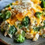 Chicken broccoli casserole protein - the image is a close-up of a plate of food. the plate is brown and has a speckled pattern around the edges. on top of the plate, there is a layer of shredded cheese, which appears to be a combination of orange and yellow colors. the cheese is melted and bubbly, and there are small pieces of broccoli scattered throughout the dish. the broccoli is bright green and looks fresh and healthy. the dish looks appetizing and ready to eat.