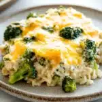 Chicken broccoli rice casserole greek yogurt - the image shows a plate of food with a casserole dish on it. the dish appears to be made with rice, broccoli, and cheese. the rice is white and fluffy, and the broccoli is bright green. the cheese is melted and bubbly, and it looks like it has been cooked until it is golden brown. the plate is sitting on a white countertop, and there is another dish visible in the background.