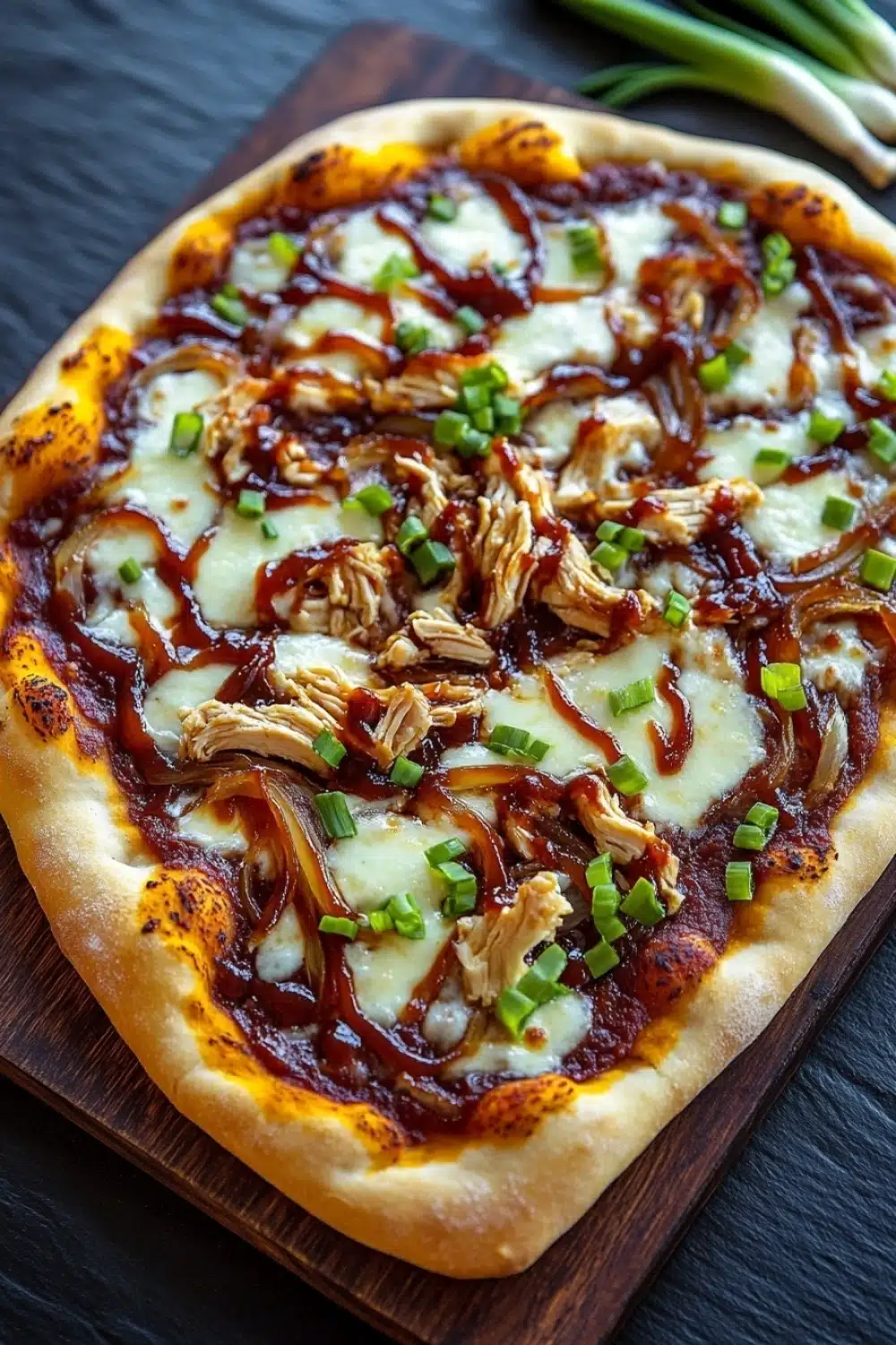 Detroit style bbq chicken pizza - the image is of a freshly baked pizza on a wooden cutting board. the pizza has a golden brown crust and is topped with melted cheese, shredded chicken, and chopped green onions. the cheese is melted and bubbly, and the chicken appears to be cooked until it is golden brown. the green onions are scattered on top of the cheese, adding a pop of color to the dish. the cutting board is placed on a dark wooden table, and there are a few sprigs of fresh green onions in the background.
