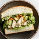 Japanese chicken salad sandwich - the image shows a sandwich in a brown ceramic bowl. the sandwich is made with two slices of white bread and is filled with a variety of vegetables, including lettuce, carrots, and cucumbers. the vegetables are arranged in a way that they are overlapping each other, creating a colorful and appetizing presentation. the bread appears to be soft and fluffy, and the vegetables are bright and vibrant. the bowl is sitting on a white marble countertop.